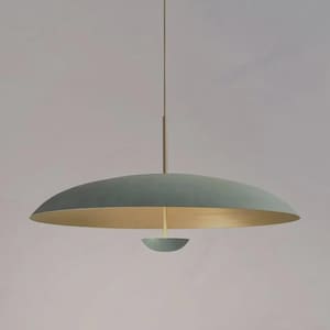 Op de afbeelding: Een hanglamp met een brede, ondiepe, mat saliegroene koepelvormige kap met een metallic gouden binnenkant. Een dunne verticale stang hangt de kap op, die is geaccentueerd met een kleine, bijpassende saliegroene halfronde dop aan de onderzijde.