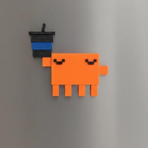 May include: An orange pixelated creature magnet with a black and blue coffee cup. The magnet is attached to a silver refrigerator door. The creature has two curved eyebrows and four legs.