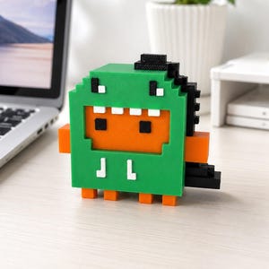 May include: A pixelated green dinosaur figurine with an orange face, black eyes, and white teeth. The figure features a black spine, orange side arms, and orange feet. It is constructed from blocky, layered components with a distinct grid-like texture.