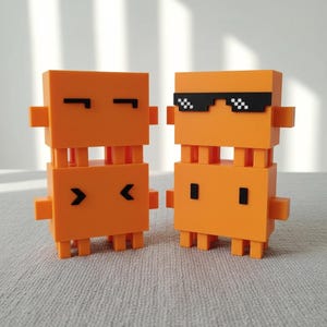 Peut inclure: Deux figurines orange en blocs pixélisés avec des détails noirs. L'une a les yeux fermés, l'autre porte des lunettes de soleil pixélisées. Les figurines ont des corps rectangulaires, de petites jambes et des bras, ressemblant à des personnages de jeux vidéo rétro.