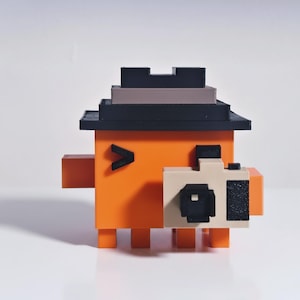 May include: A 3D-printed orange block figure with a black hat, a black V-shaped eye, and a camera. The camera is beige and black. The figure has small orange rectangular feet and arms. The hat is black, gray, and black.