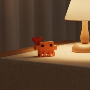 Puede incluir: Una peque&ntilde;a figura de criatura naranja pixelada con un cuerpo en bloques, cuatro patas y dos ojos cuadrados negros. Una forma de coraz&oacute;n rojo pixelado est&aacute; unida al lado superior izquierdo de la criatura, extendi&eacute;ndose hacia arriba desde su cabeza.
