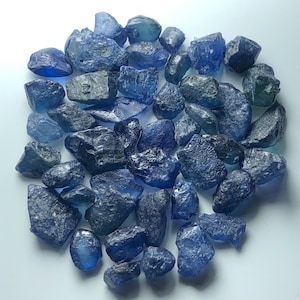 Peut inclure: Une collection de saphirs bruts et non polis dans diverses nuances de bleu profond, allant du bleu ciel clair au bleu marine foncé. Les pierres présentent des formes irrégulières et dentelées avec des textures et des facettes naturelles.