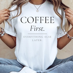 May include: A white short-sleeved t-shirt featuring the black text COFFEE First. followed by a horizontal line and the text EVERYTHING ELSE LATER. The shirt has a crew neckline and a standard fit, providing a clean look with bold typography.