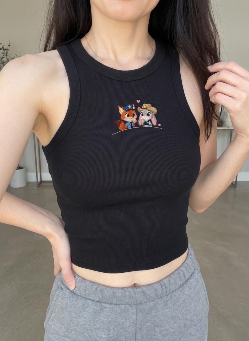 May include: Black ribbed tank top featuring an embroidered design of a fox and a bunny, each wearing a hat. The tank top has a round neckline and a fitted silhouette. The design includes a small pink heart above the characters.