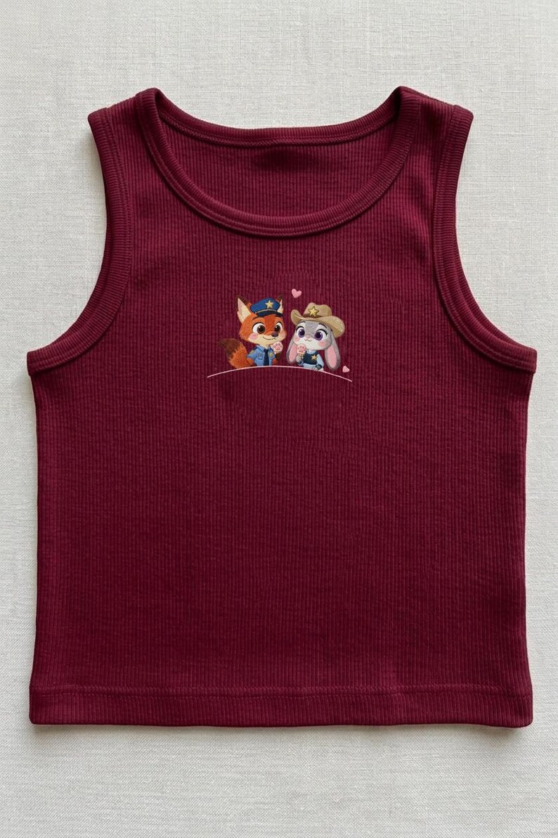May include: A burgundy ribbed tank top with a crew neck. The tank top features an embroidered design of a fox and a bunny, both wearing hats. The fox is wearing a police hat, and the bunny is wearing a cowboy hat. Two small pink hearts are above the characters.