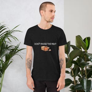 May include: Dark gray t-shirt with the text "DON'T RAISE THE RENT" above a cartoon illustration of a box with a tomato and other items. The shirt is short-sleeved and has a crew neck.