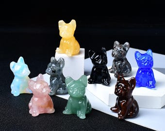 May include: A collection of small, gemstone bulldog figurines in various colors, including yellow, blue, black, and green. The figurines are displayed on a white surface against a dark background. Each dog is carved with detail, showcasing the natural beauty of the stones.