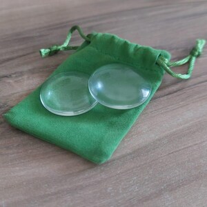 Könnte beinhalten: Zwei klare, kreisförmige und glatte Glaskabochons liegen auf einem kleinen, leuchtend grünen Stoffbeutel mit Kordelzug. Der Beutel verfügt über einen passenden grünen Kordelverschluss an der Oberseite und bietet eine einfache Aufbewahrungslösung.