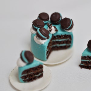May include: A miniature chocolate cake with turquoise frosting and chocolate cookie decorations. The cake is cut into slices and served on white plates.
