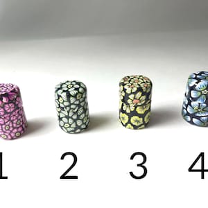 May include: Four small, round containers with floral patterns. The containers are black with white, pink, yellow, and blue flowers. The containers are numbered 1 through 4.