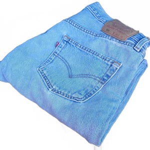 May include: Light blue denim jeans featuring a classic five-pocket design, a rear patch pocket with stitched arcuate detailing, a small red brand tab, and a brown leather-like waistband patch clearly displaying the text 501 W 36 L 34.