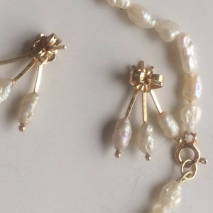 May include: A pair of gold earrings with three white pearls dangling from each earring. The earrings are attached to a gold chain with a clasp.