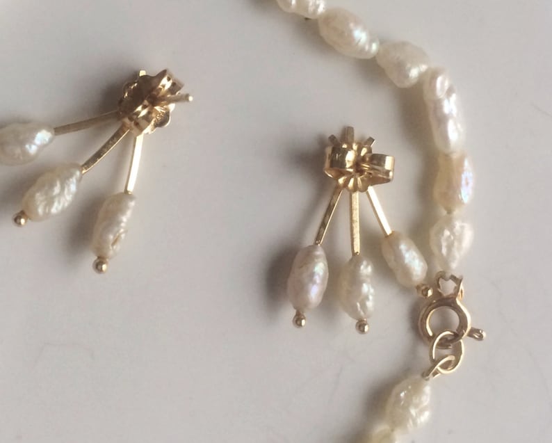 May include: A pair of gold earrings with three white pearls dangling from each earring. The earrings are attached to a gold chain with a clasp.