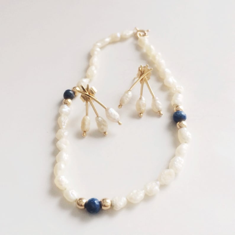 May include: A white pearl necklace with blue gemstone accents and matching earrings. The necklace and earrings feature a gold-tone design with multiple pearls hanging from each earring.