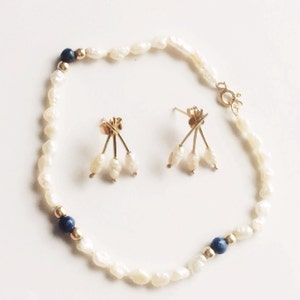 May include: A set of pearl earrings and a pearl bracelet with blue accents. The earrings feature three pearls dangling from a gold setting. The bracelet is made of white pearls and has two blue stones.