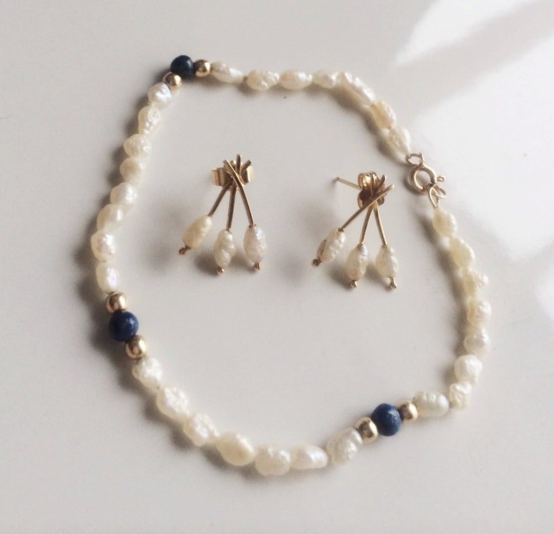 May include: A set of pearl earrings and a pearl bracelet with blue accents. The earrings feature a gold design with three pearls dangling from each earring. The bracelet is made of white pearls with two blue beads.