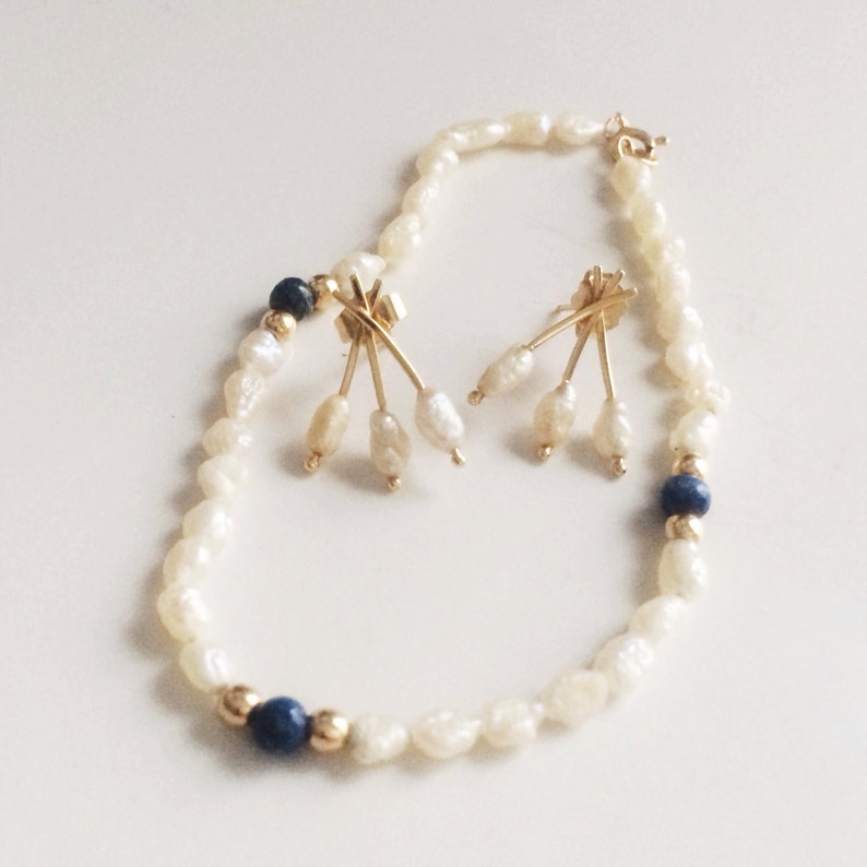 May include: A pearl bracelet with gold accents and blue beads. The bracelet is paired with a set of pearl earrings with gold accents.