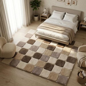 May include: A bedroom scene with a large rug featuring a square block pattern in beige, brown, and grey. The rug is on a wooden floor, with a bed, chairs, and a basket. The room is well-lit with natural light, creating a warm and inviting atmosphere.