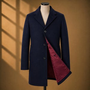 May include: A navy blue overcoat featuring a notched lapel, three front buttons, and long sleeves. The coat is displayed on a mannequin and is partially open, revealing a smooth, deep burgundy red lining on the interior of the front panel.