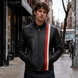 May include: A black leather jacket featuring a stand-up collar, a central zipper closure, and a vertical racing stripe in red and cream running down the left side. The jacket includes a horizontal zippered chest pocket and two side pockets.