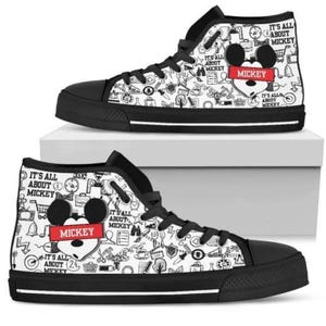 Puede incluir: Zapatillas altas de lona con suela y cordones negros. La lona blanca est&aacute; cubierta de garabatos negros y el texto "IT'S ALL ABOUT MICKEY". Una cabeza de Mickey Mouse con el nombre "MICKEY" en un rect&aacute;ngulo rojo aparece en el lateral.