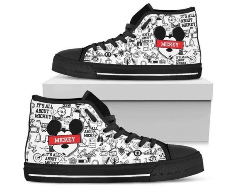Puede incluir: Zapatillas altas de lona con suela y cordones negros. La lona blanca est&aacute; cubierta de garabatos negros y el texto "IT'S ALL ABOUT MICKEY". Una cabeza de Mickey Mouse con el nombre "MICKEY" en un rect&aacute;ngulo rojo aparece en el lateral.