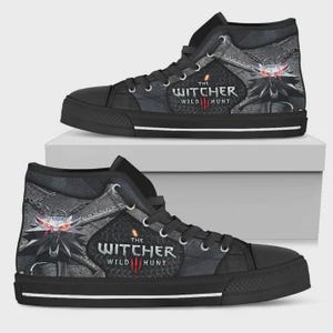 May include: A pair of black high-top sneakers featuring The Witcher Wild Hunt logo and a wolf medallion graphic with glowing red eyes. The shoes have black laces, a black rubber toe cap, and a white stripe along the base of the black sole.