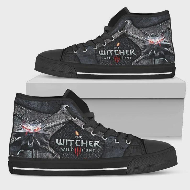 May include: A pair of black high-top sneakers featuring The Witcher Wild Hunt logo and a wolf medallion graphic with glowing red eyes. The shoes have black laces, a black rubber toe cap, and a white stripe along the base of the black sole.