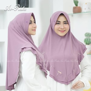 Peut inclure: Deux femmes portant des hijabs lavande assortis. Les hijabs présentent des perles décoratives et un design plissé. Les femmes portent des hauts blancs. L'image contient le texte "Ar-Rista".