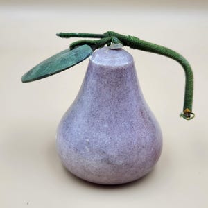 May include: A pear-shaped decorative object made of smooth, mottled light purple stone. It features a dark green, fabric-wrapped stem extending to the right and a single, flat, dark green leaf attached to the top of the stone fruit body.
