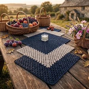 May include: A rustic wooden picnic table is set with a variety of items. Wicker baskets hold fruit and flowers. A blue and beige crocheted placemat is in the center. A candle, nuts, and a mug complete the scene.