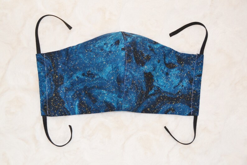 K&ouml;nnte beinhalten: Eine blaue und goldene Gesichtsmaske mit Marmormuster. Die Maske hat schwarze elastische Ohrschlaufen.