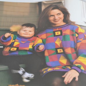 K&ouml;nnte beinhalten: Eine Frau und ein Kind tragen bunte Pullover mit geometrischen Mustern. Die Frau sitzt auf einer Treppe und das Kind steht auf den Stufen. Die Frau tr&auml;gt einen schwarzen Rock und das Kind tr&auml;gt eine blaue Hose.