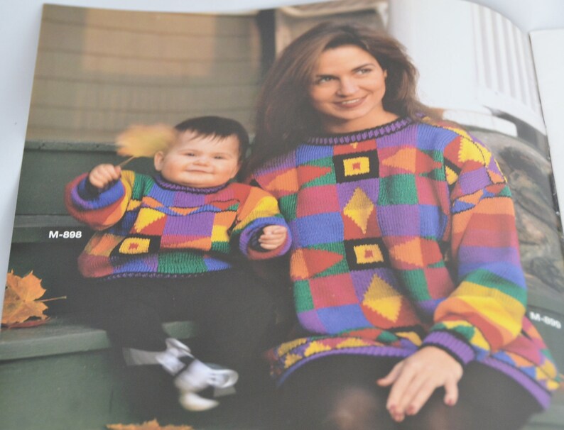 K&ouml;nnte beinhalten: Eine Frau und ein Kind tragen bunte Pullover mit geometrischen Mustern. Die Frau sitzt auf einer Treppe und das Kind steht auf den Stufen. Die Frau tr&auml;gt einen schwarzen Rock und das Kind tr&auml;gt eine blaue Hose.