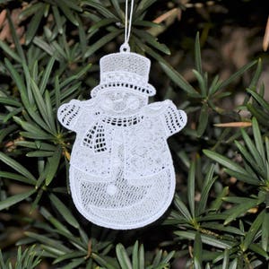 Pode incluir: Adorno de Natal de boneco de neve branco de croch&ecirc; com chap&eacute;u e cachecol. O adorno est&aacute; pendurado em um galho de &aacute;rvore.