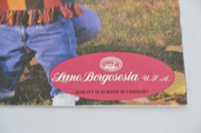 K&ouml;nnte beinhalten: Ein rotes ovales Etikett mit wei&szlig;em Text, der "Lamo Borgosesia U.P.A. QUALITY IS ALWAYS IN FASHION" lautet.