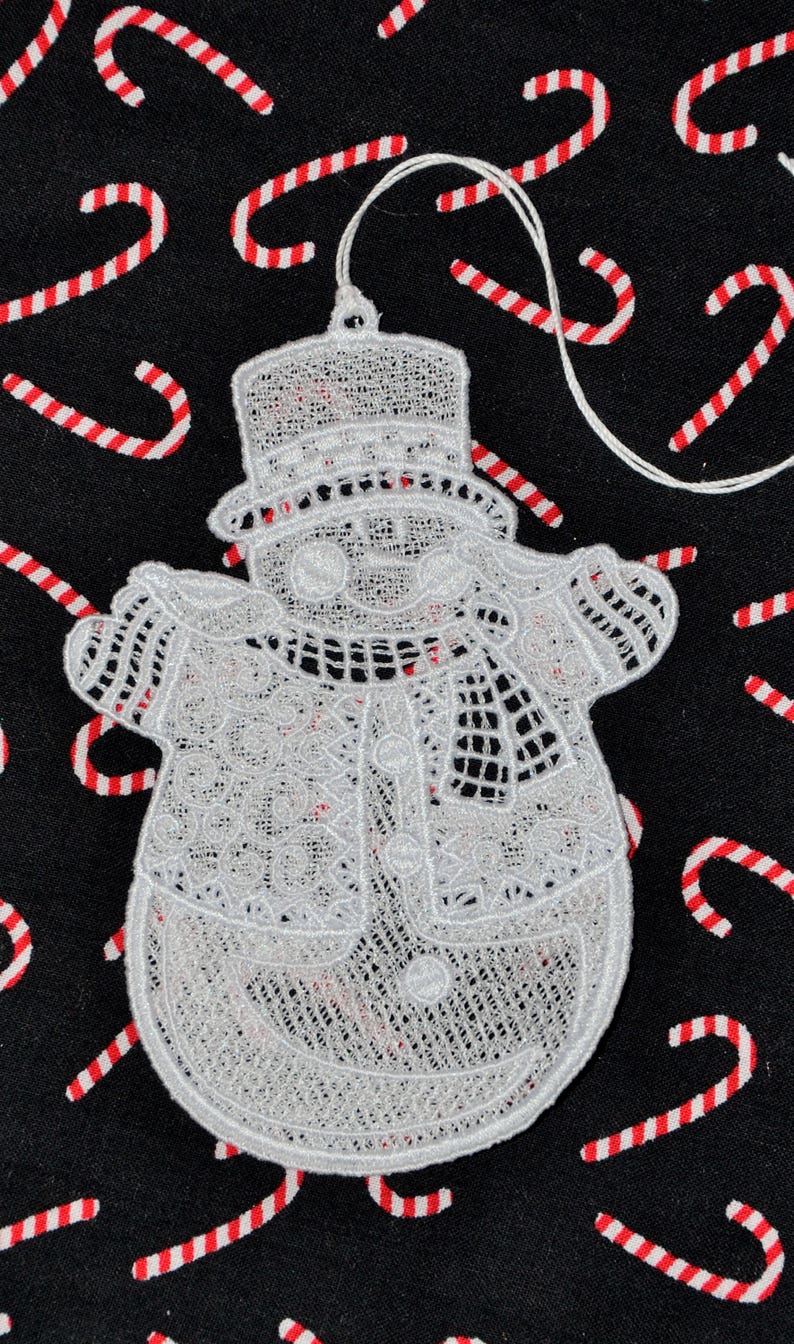Pode incluir: Adorno de Natal de boneco de neve branco de croch&ecirc; em fundo preto. O boneco de neve tem um chap&eacute;u, uma echarpe e um bot&atilde;o.