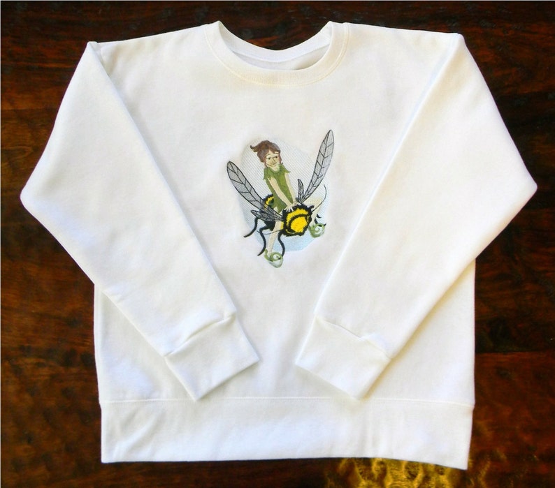 May include: White sweatshirt with a green fairy riding a yellow and black bee embroidered on the front.