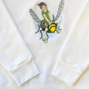 May include: White sweatshirt with a graphic of a fairy riding a bee. The fairy is wearing a green dress and has brown hair. The bee is yellow and black with wings.