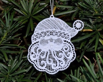 Pode incluir: Adorno de Natal de renda branca em forma de rosto do Papai Noel com barba e chapéu.