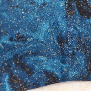 K&ouml;nnte beinhalten: Nahaufnahme eines dunkelblauen Stoffes mit einem verstreuten Muster aus goldenen Glitzer. Der Stoff hat einen dezenten Marmoreffekt.