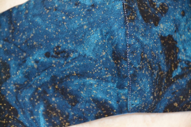 K&ouml;nnte beinhalten: Nahaufnahme eines dunkelblauen Stoffes mit einem verstreuten Muster aus goldenen Glitzer. Der Stoff hat einen dezenten Marmoreffekt.