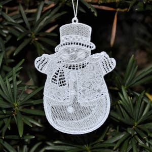 Pode incluir: Ornamento de boneco de neve de renda branca com um design detalhado. O boneco de neve est&aacute; usando um chap&eacute;u e uma echarpe.