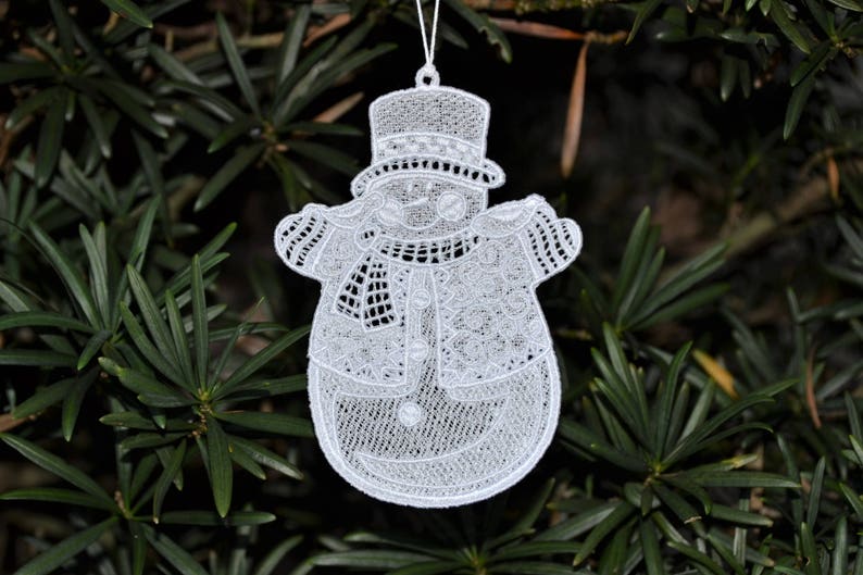 Pode incluir: Ornamento de boneco de neve de renda branca com um design detalhado. O boneco de neve est&aacute; usando um chap&eacute;u e uma echarpe.