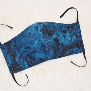 K&ouml;nnte beinhalten: Eine blaue und goldene Gesichtsmaske mit Marmormuster. Die Maske hat schwarze elastische B&auml;nder.