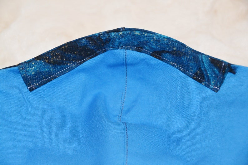 K&ouml;nnte beinhalten: Nahaufnahme der Oberseite einer blauen Stoffmaske mit einem dunkelblauen und goldfarbenen Muster.