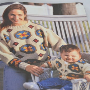 K&ouml;nnte beinhalten: Eine Frau und ein Kind tragen passende Pullover mit einem geometrischen Muster in Blaut&ouml;nen, Gelb, Rot und Braun. Die Pullover haben einen cremefarbenen Hintergrund. Die Frau tr&auml;gt eine blaue Jeans und das Kind tr&auml;gt eine blaue Jeans.