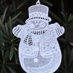 Pode incluir: Adorno de Natal de boneco de neve branco em croch&ecirc; com um chap&eacute;u-coco preto e uma echarpe branca. O adorno est&aacute; pendurado em um cord&atilde;o branco.