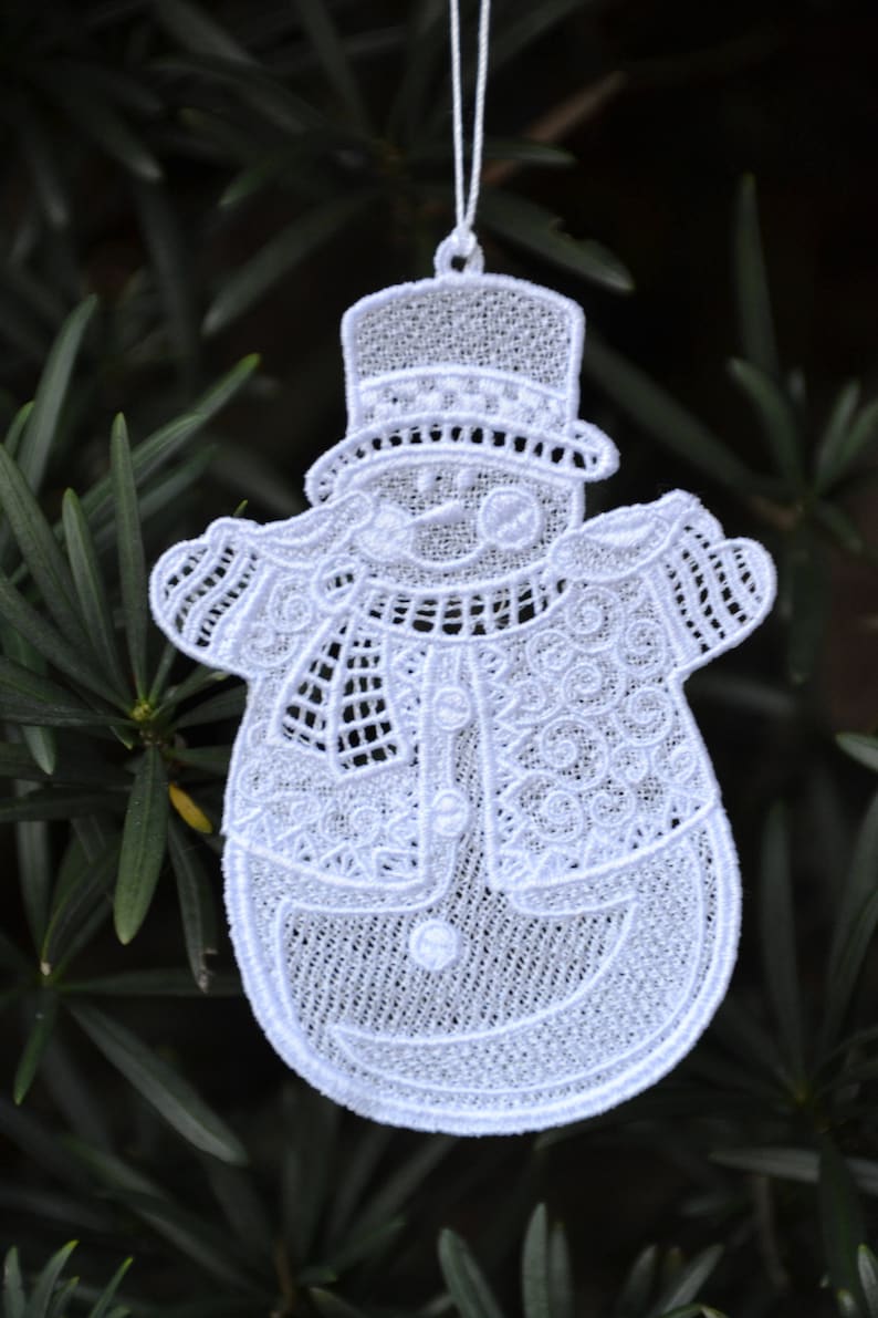 Pode incluir: Adorno de Natal de boneco de neve branco em croch&ecirc; com um chap&eacute;u-coco preto e uma echarpe branca. O adorno est&aacute; pendurado em um cord&atilde;o branco.